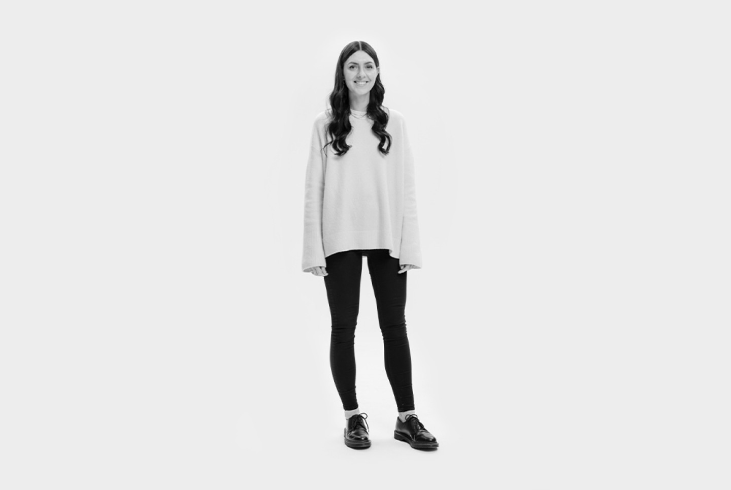 Woman with black hair in white top and black jeans stood.